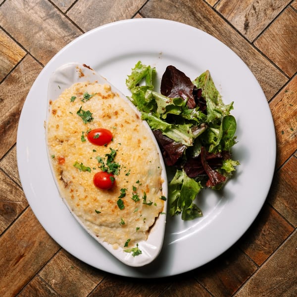 Shepherd's pie with a golden-brown crust, garnished with cherry tomatoes and parsley, served with a side salad.