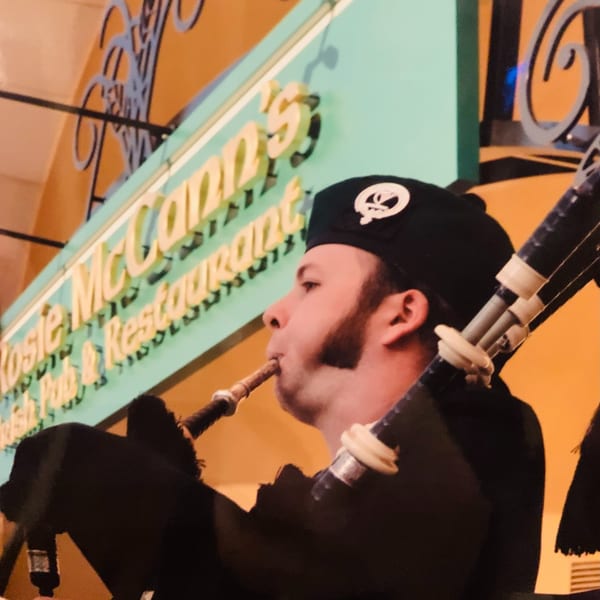 A man in a black beret playing bagpipes in front of the Rosie McCann's Irish Pub sign.
