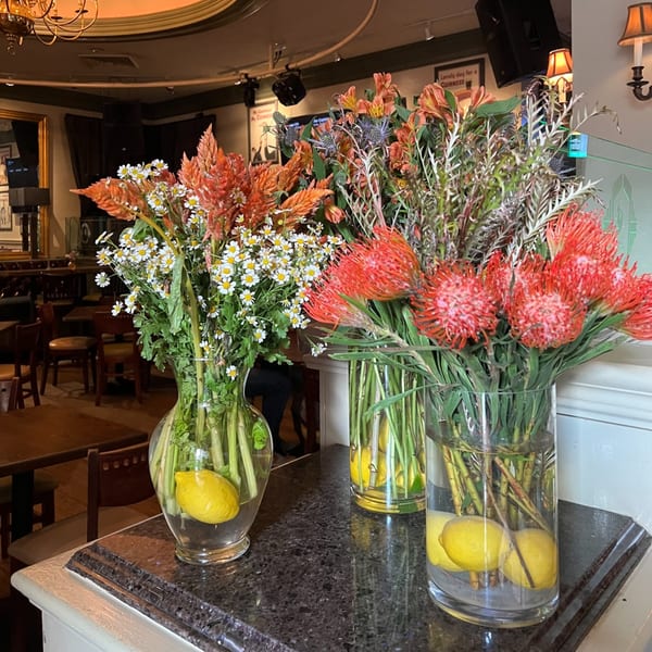Three vases with lemons and vibrant flower arrangements, including red, orange, and white blooms, on a dark counter.