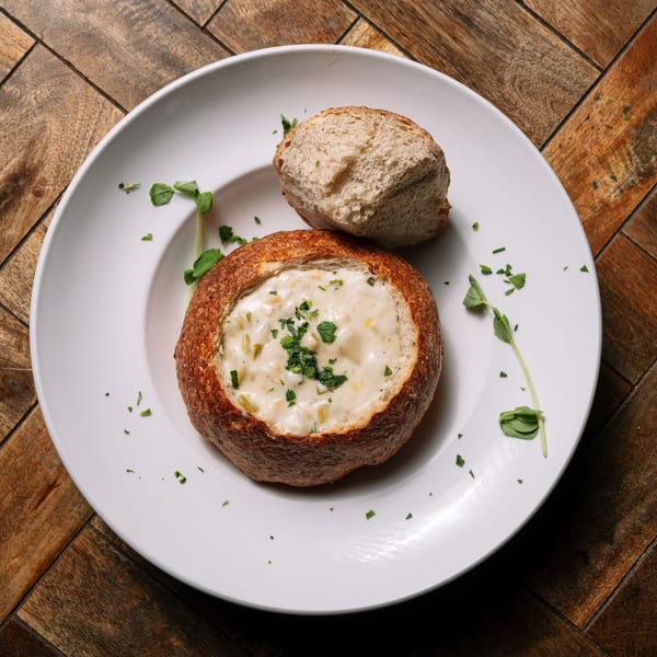 Creamy Irish seafood chowder in a bread bowl with a side of bread on a white plate.