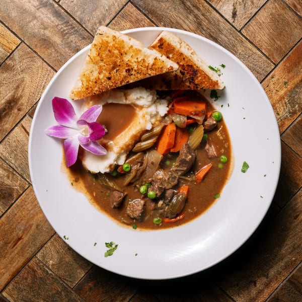 Rosie McCann's Irish stew with mashed potatoes, gravy, vegetables, and toasted bread, garnished with an orchid.