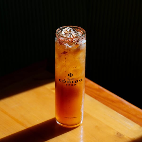 Tall glass of orange drink with a spiced rim and lime slice on a wooden table.