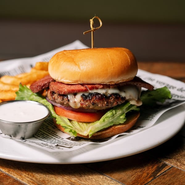 A Rosie McCann's burger with bacon, cheese, lettuce, tomato, and a side of fries and dip.